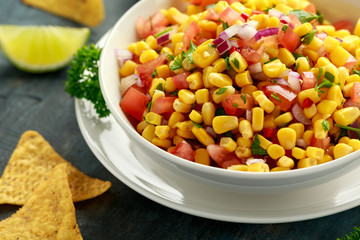 Mexican Corn Salsa in white bowl with lime and tortilla chips. Healthy food