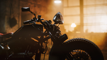 Kundenspezifisches Bobber-Motorrad, das in einer authentischen Kreativwerkstatt steht. Motorrad im Vintage-Stil unter warmem Lampenlicht in einer Garage. Profilansicht.