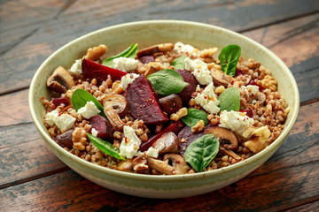 Buckwheat and beetroot salad with mushroom, walnut, spinach and feta cheese on rustic wooden table. healthy diet food
