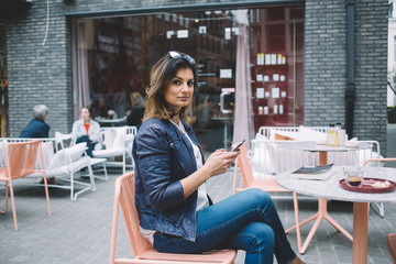 Confident woman using smartphone in sidewalk cafe