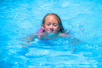 Pretty young girl swimming with goggles outdoors in swimming pool. Summer holiday and happy carefree childhood concept.