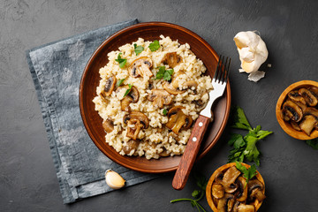 A dish of Italian cuisine - risotto from rice and mushrooms in a brown plate on a black slate background. Above view.