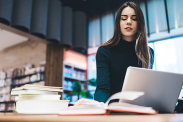 Smart woman with laptop reading book in library