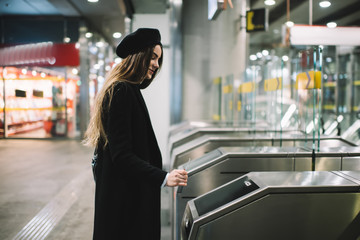 Positive woman in warm outerwear going through turnstile in subway
