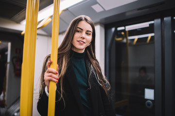 Positive young woman in warm casual wear inside subway train