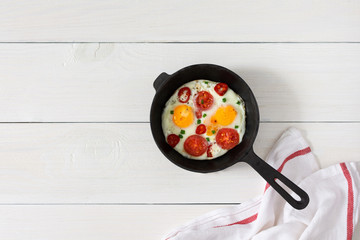 Fresh delicious breakfast of eggs and tomatoes with spices and red pepper, frying pan with fried eggs on white wooden background, top view, copy space
