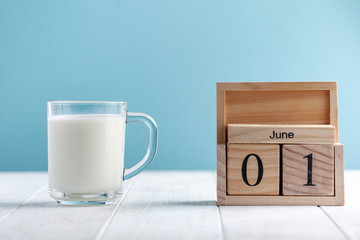  Wooden calendar June 1, a mug of milk on a blue background. The concept of Milk Day, Children's Day, June 1.Copy space.