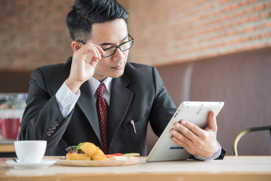 Businessman wearing eyeglasses looking information on tablet.