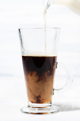milk is poured into a glass cup with black coffee