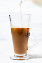 milk is poured into a glass cup with coffee