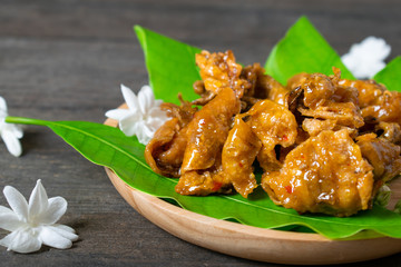 Fried dried squid on mango leaves in wooden dish.