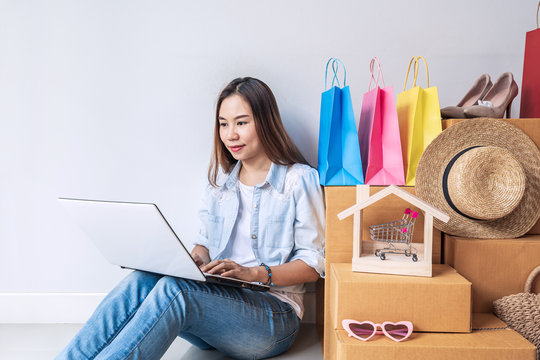 Young asian woman with colorful shopping bag, fashion items and stack of cardboard boxes at home, Website online shopping concept with copy space