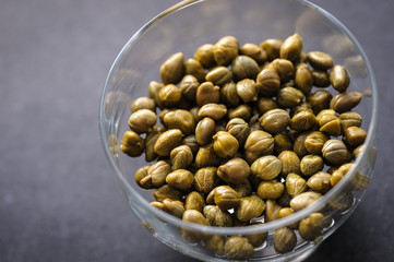 pickled capers in a glass bowl on a dark background, top view close up