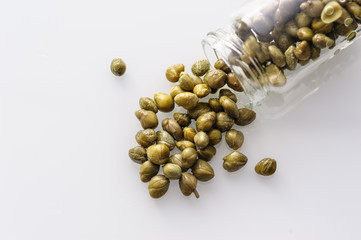 scattered pickled capers on a white plate, top view close-up