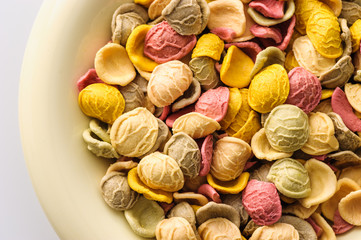 uncooked colored homemade pasta in a bowl close-up on a white table, top view
