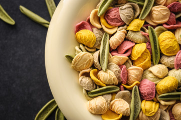 uncooked colored homemade pasta in a bowl close-up on a dark table, top view