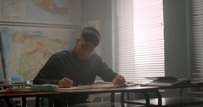 Young student studying and taking notes in classroom surrounded by warm daylight