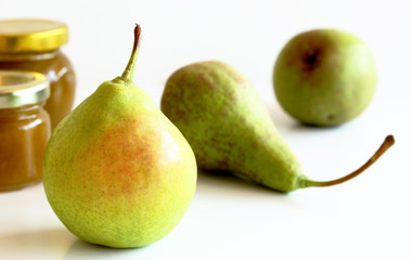 Glass jar of homemade pear jam with fresh juicy fruits in the form of ingredients, isolated on white background. Delicious fruit. Blurred background.Food and healthy concept.