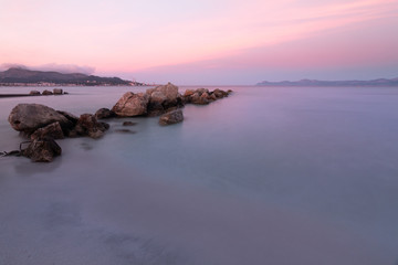 Fototapeta na wymiar Rocks lined up on the shoreline with silky water at sunset and mountains in the background