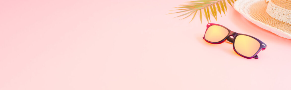 summer accessories concept from sunglasses, straw hat and palm leaf on pastel pink background, for banner advertising.