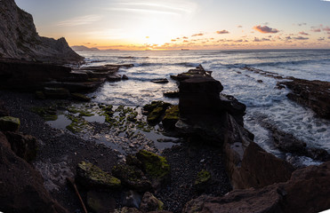 Paisaje de playa de rocas en Punta Galea con acantilados y barcos en el fondo del paisaje con una puesta de sol muy bonita