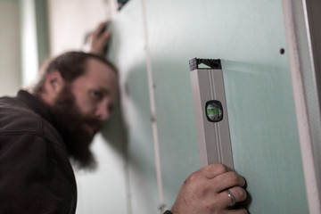 Hendwerker mit Bart prüft die Ausrichtung der Wände aus Gipsplatte mit einer Wasserwaage