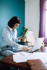 Beautiful woman working on a laptop at home. Attractive freelancer using laptop and drinking coffee. The girl chatting with friends in social network, shopping online, writing email.