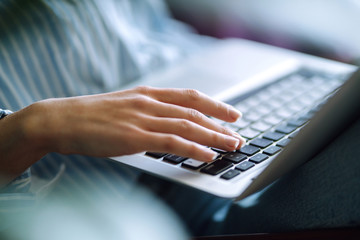 Close up picture of females hands on the keyboard. Young woman working with laptop sitting in modern living room at home. Technology, freelance and work concept.