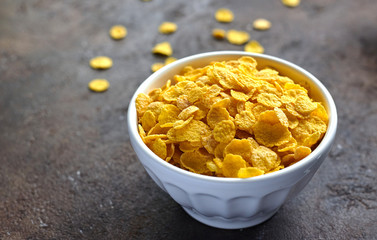 yellow dry corn flakes in a white deep plate on a brown table