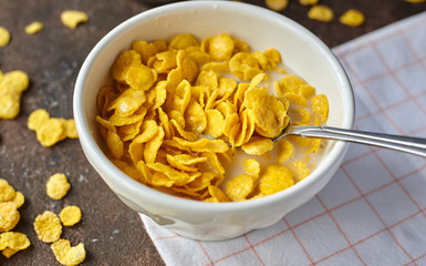 yellow cornflakes with milk in a white deep plate on a brown table