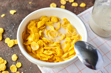 yellow cornflakes with milk in a white deep plate on a brown table