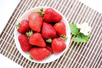 ripe strawberries on a white plate and jasmine flowers. still life