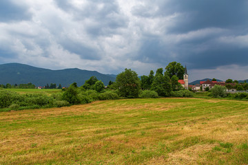 Fototapeta na wymiar Landscape with mountains and the village of Pudob with a nice catholic church in the Inner Carniola region, Slovenia