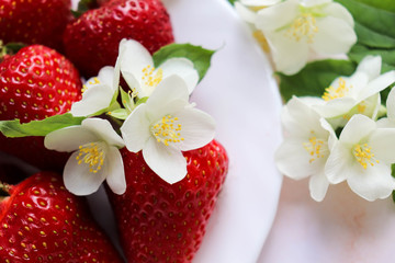 ripe strawberries on a white plate and jasmine flowers. still life