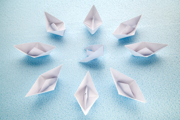 A sinking paper boat is surrounded by surviving boats awaiting help.