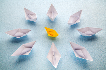 One yellow paper boat is surrounded by many large white boats. - 352233548