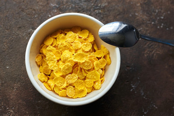 yellow dry corn flakes in a white deep plate on a brown table