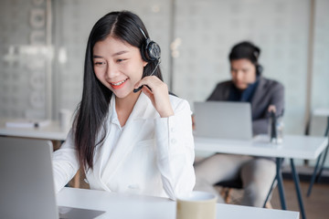 Attractive young asian female call center agent in headset consulting client. Customer service team...