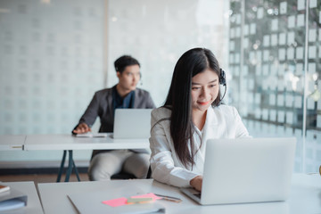 Attractive young asian female call center agent in headset consulting client. Customer service team support concept
