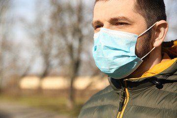 Man wearing disposable mask outdoors, closeup. Dangerous virus