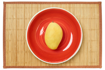 pale yellow mango on a red plate on a cane place mat