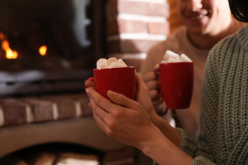 Lovely couple with sweet cocoa near fireplace indoors, closeup