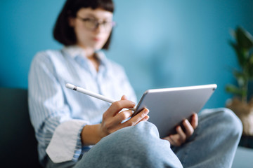 Woman using digital tablet with blank screen on sofa at home. The girl chatting with friends in social network, shopping online, writing email. Technology, freelance and work concept.