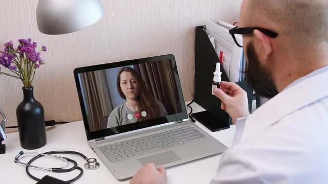 Telemedicine. Consultation with physician through mobile video call. Doctor talking to comlaining patient using video chat application on laptop and prescribes a medication