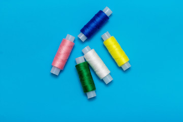white, blue, green, pink, yellow thread and turquoise ribbon on a blue background, copy space, top view