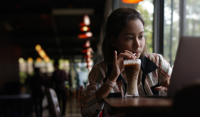 Portrait of young aisian female drinking ice coffee and thoughtfully looking out of the coffee shop window while enjoying her leisure time alone,social distancing concept.