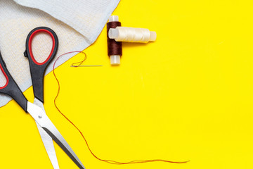 fabric, brown and beige thread, needle, scissors on a yellow Sunny background, top view, place for text, copyspace