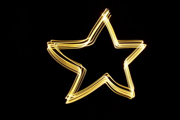 Long exposure photograph of neon gold colour in an abstract star shape outline, parallel lines pattern against a black background. Light painting photography.