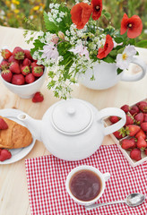 Romantic Valentines french or rural breakfast: tea, strawberries, croissants on table in poppy field. Countryside and Cozy Good morning weekend concept. Background with copy space. Date outdoors