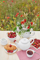 Romantic Valentines french or rural breakfast: tea, strawberries, croissants on table in poppy field. Countryside and Cozy Good morning weekend concept. Background with copy space. Date outdoors